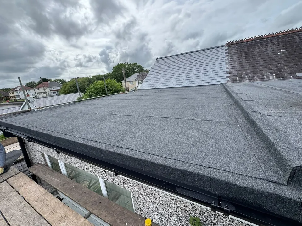 New felt flat roof on a single-storey extension with scaffold still up, beside a slate roof