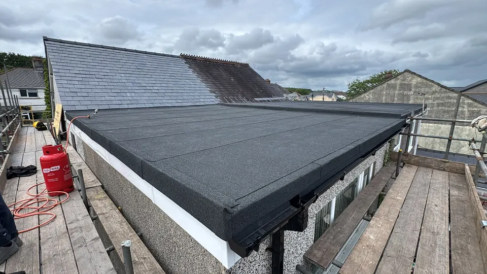 New felt flat roof with white uPVC fascia on an extension, slate roof behind
