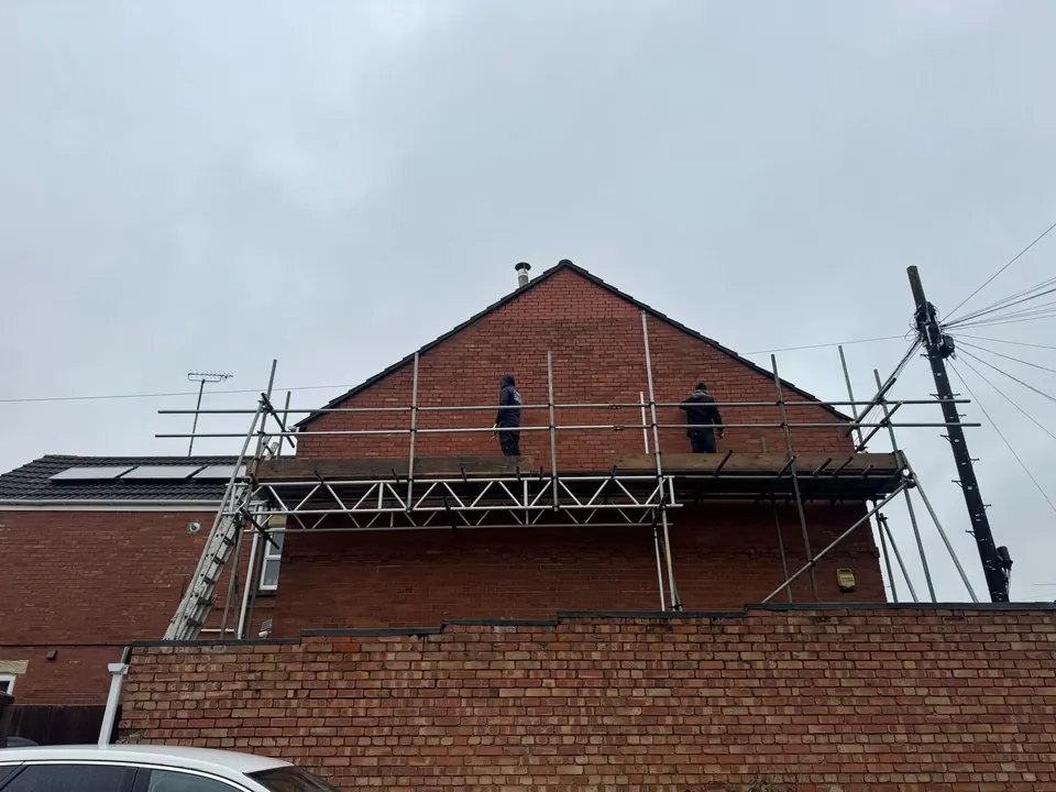 Brick gable-end house under scaffold with two roofers working along the ridge