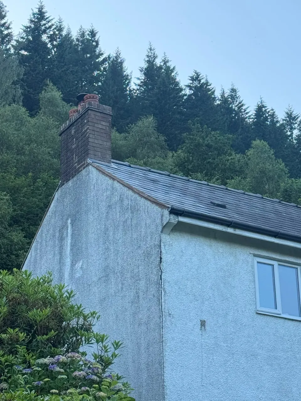 White rendered house with a slate roof and brick chimney